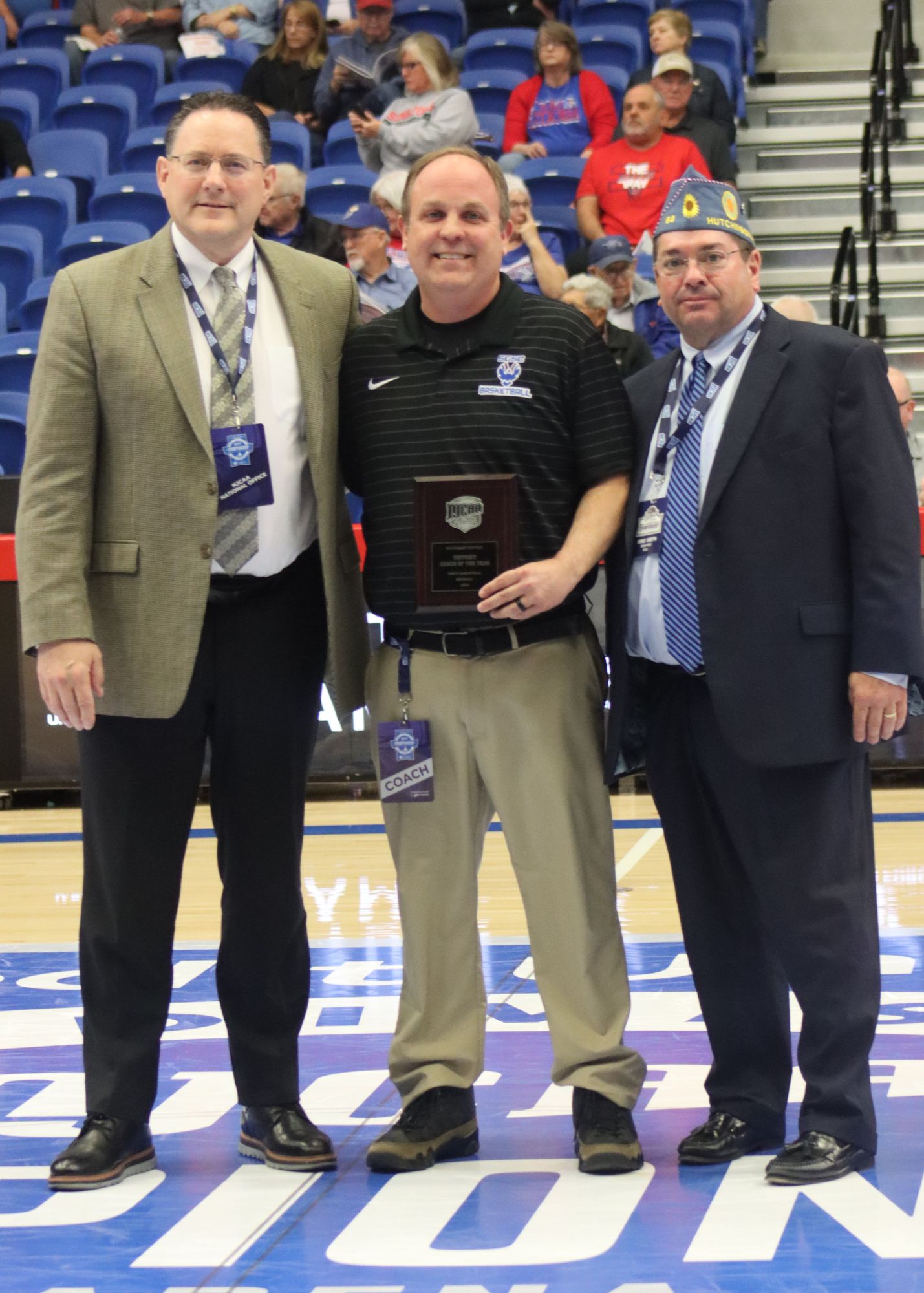 three men standing in a gym and one receiving an award